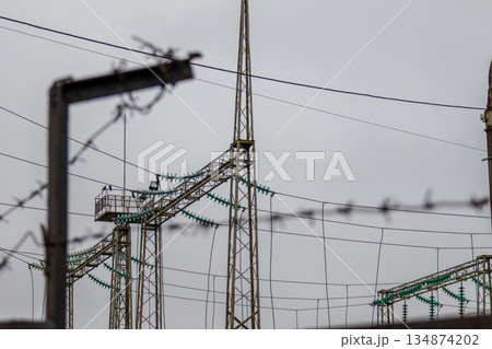 Electricity towers stand tall behind a barbed wire fence on an overcast day in an industrial zone Electricity towers stand tall behind a barbed wire fence on an overcast day in an industrial zone 134874202