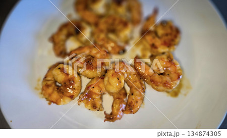 Hibachi grilled shrimp curled on white plate, brushed with a golden garlic butter glaze and teriyaki sauce. This savory seafood appetizer is perfect for gatherings, offering a warm aroma 134874305
