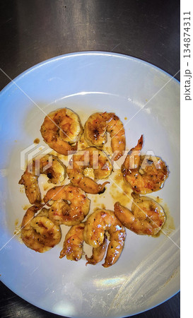Hibachi grilled shrimp curled on white plate, brushed with a golden garlic butter glaze and teriyaki sauce. This savory seafood appetizer is perfect for gatherings, offering a warm aroma 134874311