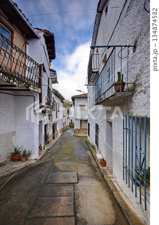 Narrow whitewashed village street with blue balconies and potted plants under a sunny sky Narrow whitewashed village street with blue balconies and potted plants under a sunny sky 134874582