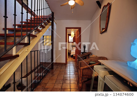Cozy hallway interior with staircase, wicker chairs, and warm lighting in a rustic home setting 134874600
