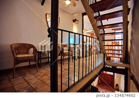 Cozy rustic interior with wicker chairs and a wooden staircase in a charming indoor cafee setting Cozy rustic interior with wicker chairs and a wooden staircase in a charming indoor cafee setting 134874602