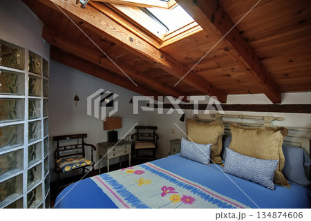 Cozy attic bedroom with skylight, wooden beams, and colorful bedspread 134874606