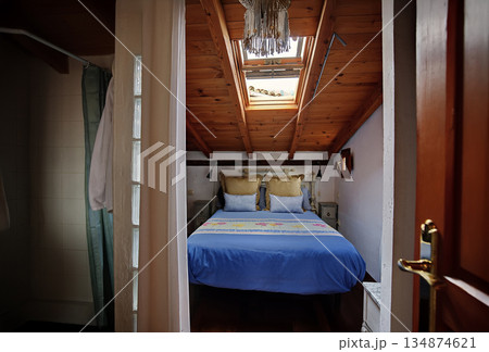 Cozy attic bedroom with blue bedspread, wooden beams, and skylight adds rustic charm 134874621