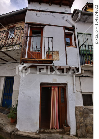 Rustic white building facade with wooden door, balcony, and potted plants on a narrow street 134874622