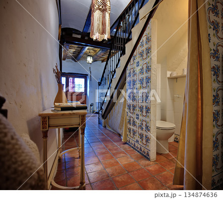 Cozy rustic hallway interior with stairs, tiled walls, and a bathroom doorway in soft warm light Cozy rustic hallway interior with stairs, tiled walls, and a bathroom doorway in soft warm light 134874636