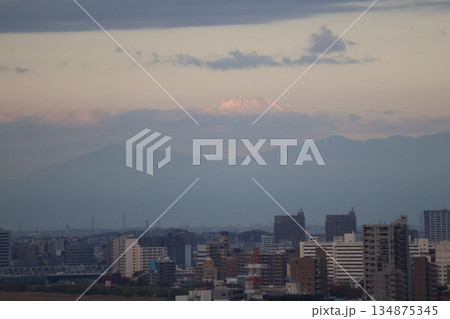 ビルのある市街地の街並みと霞む山並みと雲の上に富士山と青空の朝の風景 134875345