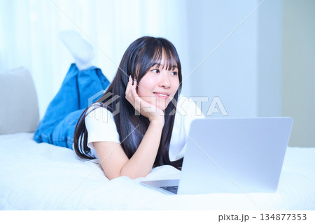 ベッドの上でリラックスしてパソコンを操作する若い女性 134877353
