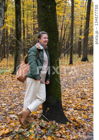 Smiling woman stands by mossy tree in Timiryazevsky Park, Moscow, surrounded by yellow autumn leaves and a calm forest mood Smiling woman stands by mossy tree in Timiryazevsky Park, Moscow, surrounded by yellow autumn leaves and a calm forest mood 134877788