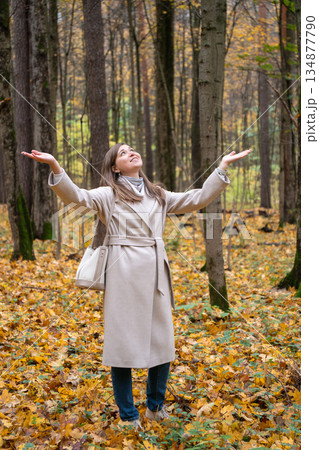 Woman standing in an autumn forest with raised arms among golden leaves in Timiryazevsky Park, Moscow, expressing hope, freedom, and making wishes Woman standing in an autumn forest with raised arms among golden leaves in Timiryazevsky Park, Moscow, expressing hope, freedom, and making wishes 134877790