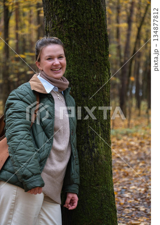 Smiling woman stands by mossy tree in Timiryazevsky Park, Moscow, surrounded by yellow autumn leaves and a calm forest mood 134877812