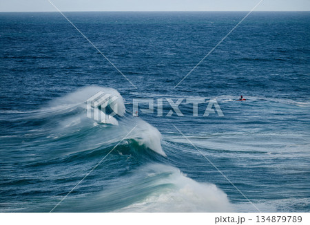 Powerful ocean waves crash as surfers ride towering swells under a clear blue sky Powerful ocean waves crash as surfers ride towering swells under a clear blue sky 134879789