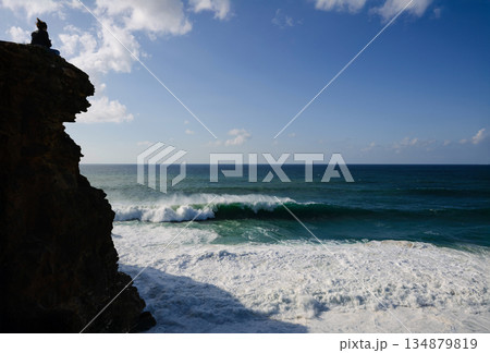Person on a cliff overlooking the ocean with waves crashing against the rocky shore Person on a cliff overlooking the ocean with waves crashing against the rocky shore 134879819