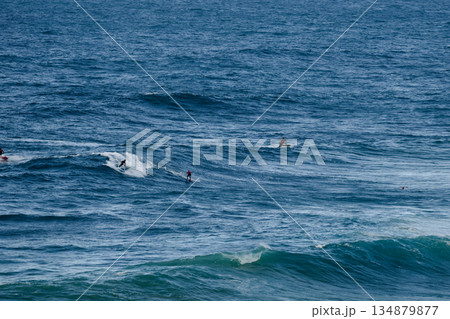 Surfers ride large blue ocean waves in an energetic open-sea scene of sport and motion Surfers ride large blue ocean waves in an energetic open-sea scene of sport and motion 134879877