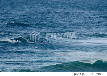Surfers riding large ocean waves together, distant riders in turquoise sea 134879889