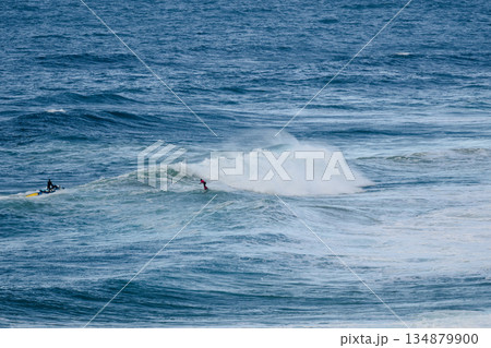 Two surfers ride a powerful wave as the ocean roars under a clear blue sky 134879900