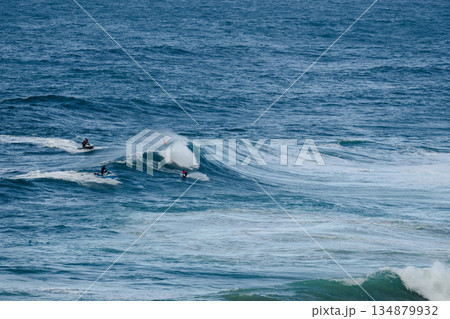 Surfers riding large ocean waves, blue water, action and motion on a sunny day at sea Surfers riding large ocean waves, blue water, action and motion on a sunny day at sea 134879932