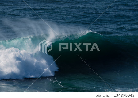 Powerful ocean wave curling over a dark turquoise sea with dramatic spray 134879945
