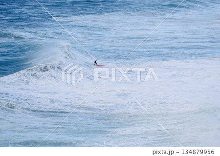 Surfer riding a large ocean wave on a bright day, balancing on a surfboard Surfer riding a large ocean wave on a bright day, balancing on a surfboard 134879956