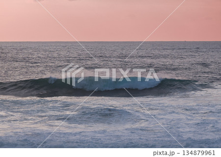 Calm ocean waves roll under a pink sunset sky over the tranquil sea 134879961