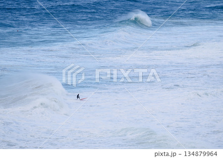 Surfer rides a massive wave in rough ocean conditions on a bright red board Surfer rides a massive wave in rough ocean conditions on a bright red board 134879964