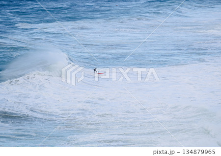 Surfer riding a large ocean wave on a bright blue sea, dynamic coastal scene 134879965