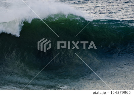 Powerful ocean wave curling over dark green water with white foam at the crest 134879966
