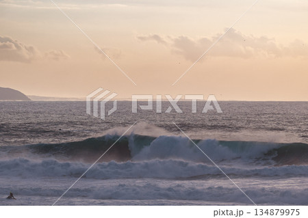 Calm ocean sunset with large waves and distant coastline, surfers nearby 134879975