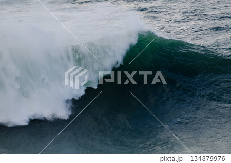 Massive ocean wave curling and breaking with white spray over deep blue water 134879976