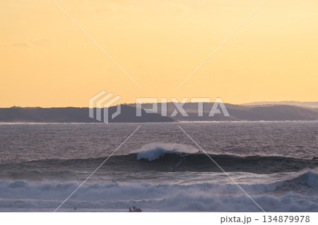 Golden hour ocean waves roll toward distant coast under warm orange sunset sky Golden hour ocean waves roll toward distant coast under warm orange sunset sky 134879978