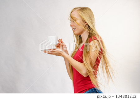 Blonde girl blowing hair holds coffee cup 134881212