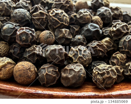 Macro Close-Up of Whole Black Peppercorns on Wooden Spoon Culinary Spice Background 134885069