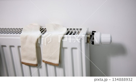 White socks drying on a radiator during the seasonal heating period. Concept of wintertime home heating, energy consumption, warmth, comfort, and everyday life in cold seasons. 134888932