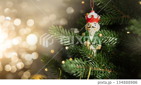 Traditional wooden nutcracker Christmas ornament hanging on a decorated Christmas tree with warm lights and golden baubles. Festive holiday atmosphere with cozy winter mood. Traditional wooden nutcracker Christmas ornament hanging on a decorated Christmas tree with warm lights and golden baubles. Festive holiday atmosphere with cozy winter mood. 134888986