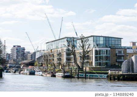 ロンドン郊外を流れるテームズ側に停泊するナローボートとマンションと遠くに見える大型クレーン 134889240