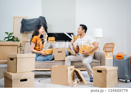 Asian young attractive couple man and woman use tablet and smartphone online shopping furniture decorate house with carton package move in new house. Young married asian moving home. 134889779