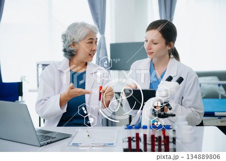 Medical team having a meeting with doctors in white lab coats and surgical scrubs seated at a table discussing a patients working online using computers 134889806