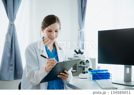Doctor in white suit take notes while discussing and Asian elderly, woman patient who lying on bed with receiving saline solution in hospital or clinic. 134889851