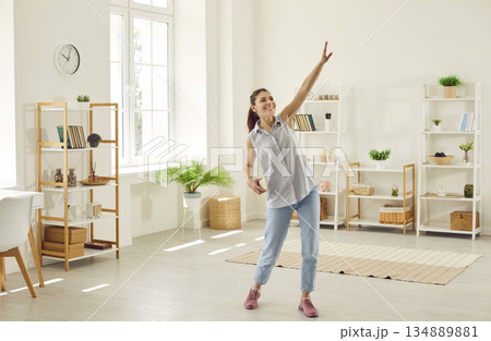 Happy young woman listening to music on her mobile phone and dancing in living room 134889881