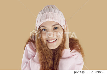 Close-up of face of beautiful smiling red-haired young woman wearing warm knitted pink hat. 134889882