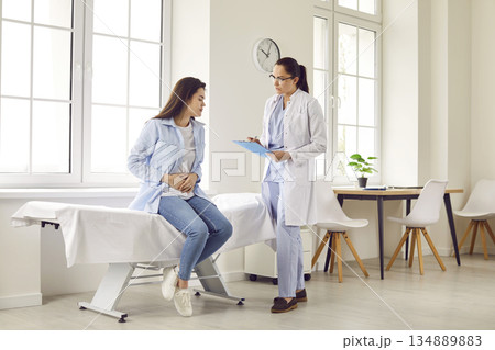 Pregnant woman with abdomen pain visiting her female obstetrician doctor in maternity clinic. 134889883