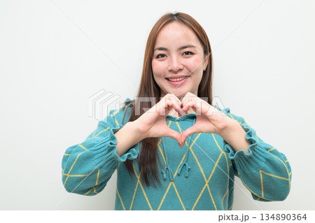 Portrait of a young Asian woman against white background making heart sign gesture 134890364