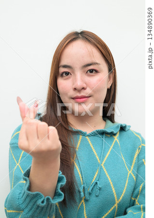 Portrait of a young Asian woman against white background making mini heart gesture Portrait of a young Asian woman against white background making mini heart gesture 134890369
