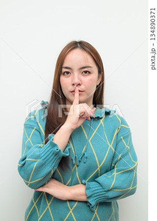 Portrait of a young Asian woman against white background with finger on lips Portrait of a young Asian woman against white background with finger on lips 134890371