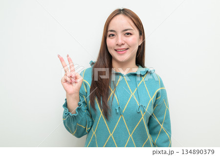 Portrait of a young Asian woman against white background making peace sign gesture 134890379
