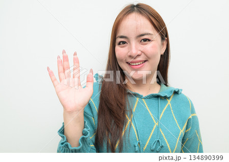 Portrait of a young Asian woman against white background waving hand in greeting 134890399