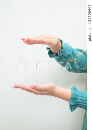 Close-up of young Asian woman against white background measuring amount with hands Close-up of young Asian woman against white background measuring amount with hands 134890405
