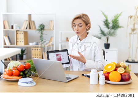 A dietitian explains the digestive system during a virtual consultation, surrounded by healthy food options. A dietitian explains the digestive system during a virtual consultation, surrounded by healthy food options. 134892091
