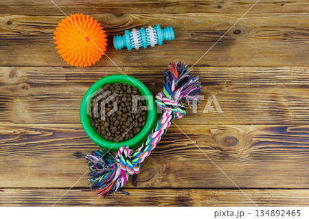 Dog toys and feed for dogs in green plastic bowl on wooden background. Top view. Dog care concept 134892465