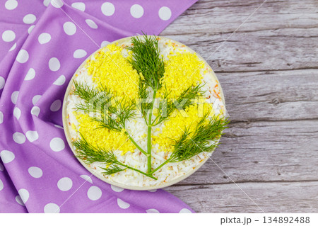 Traditional russian layered salad Mimosa decorated with sprigs of mimosa (made of eggs yolk and dill) on wooden table. Top view 134892488